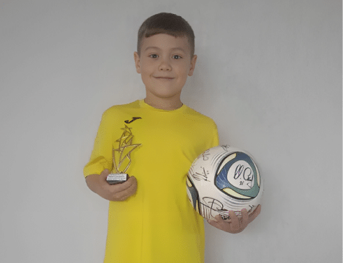 Ivan, a child, years after bone marrow transplant holding a trophy and signed football.