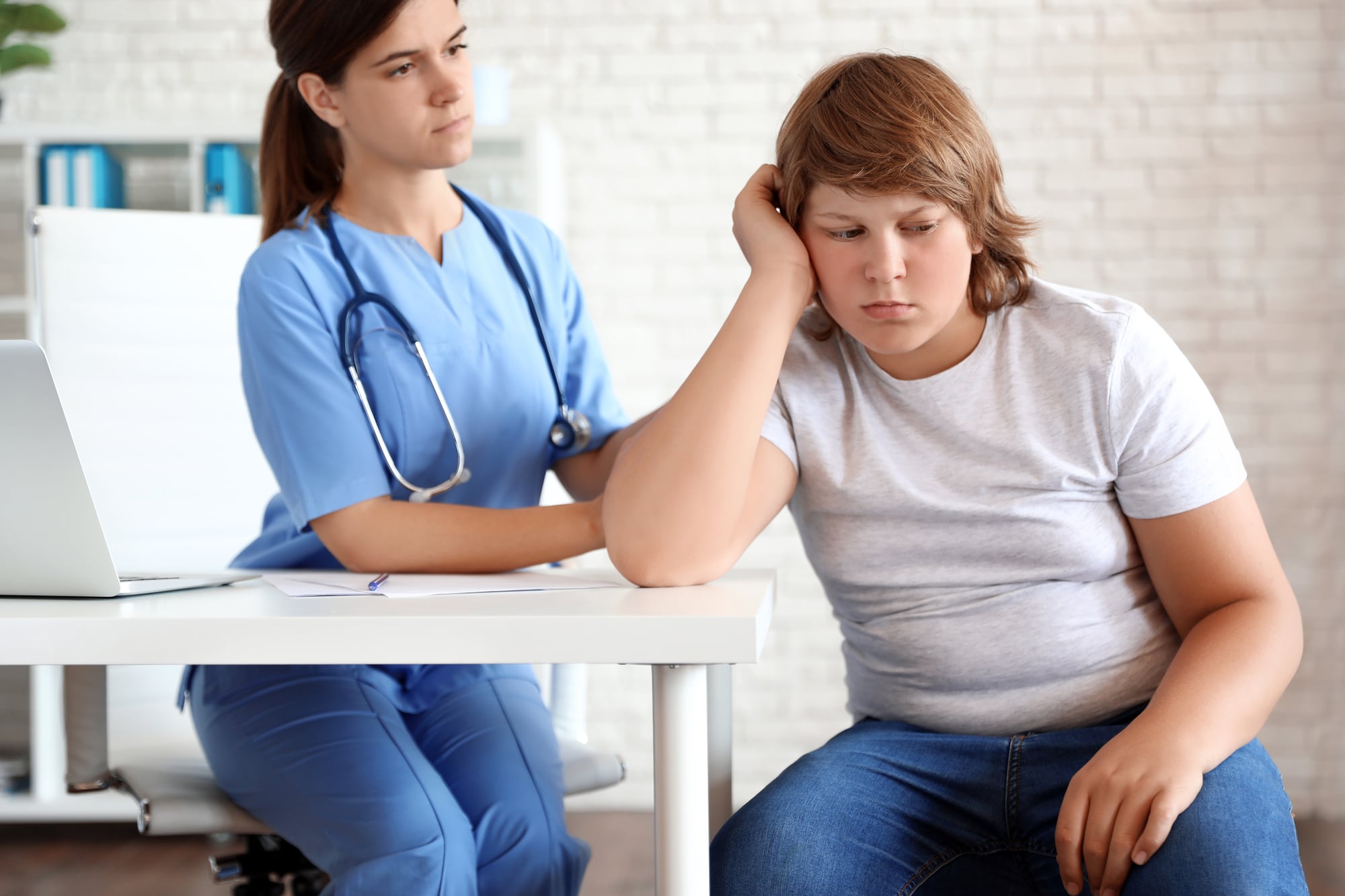 Obese teenage child pouting next to a woman doctor in a doctor's office.