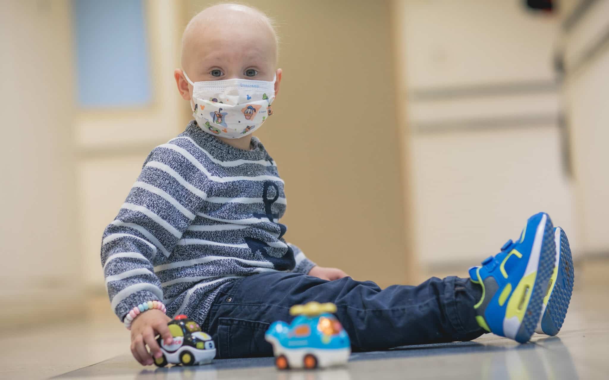 A little child with cancer wearing a cloth mask while playing with toy cars.